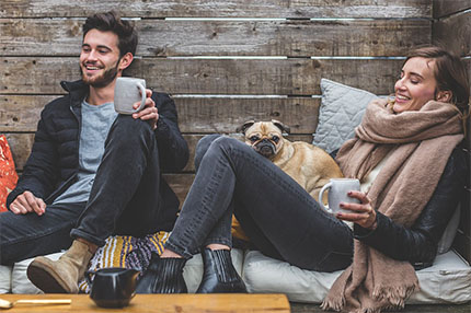 A photo of a man and a beautiful Russian woman sitting comfortably on a couch with their dog.