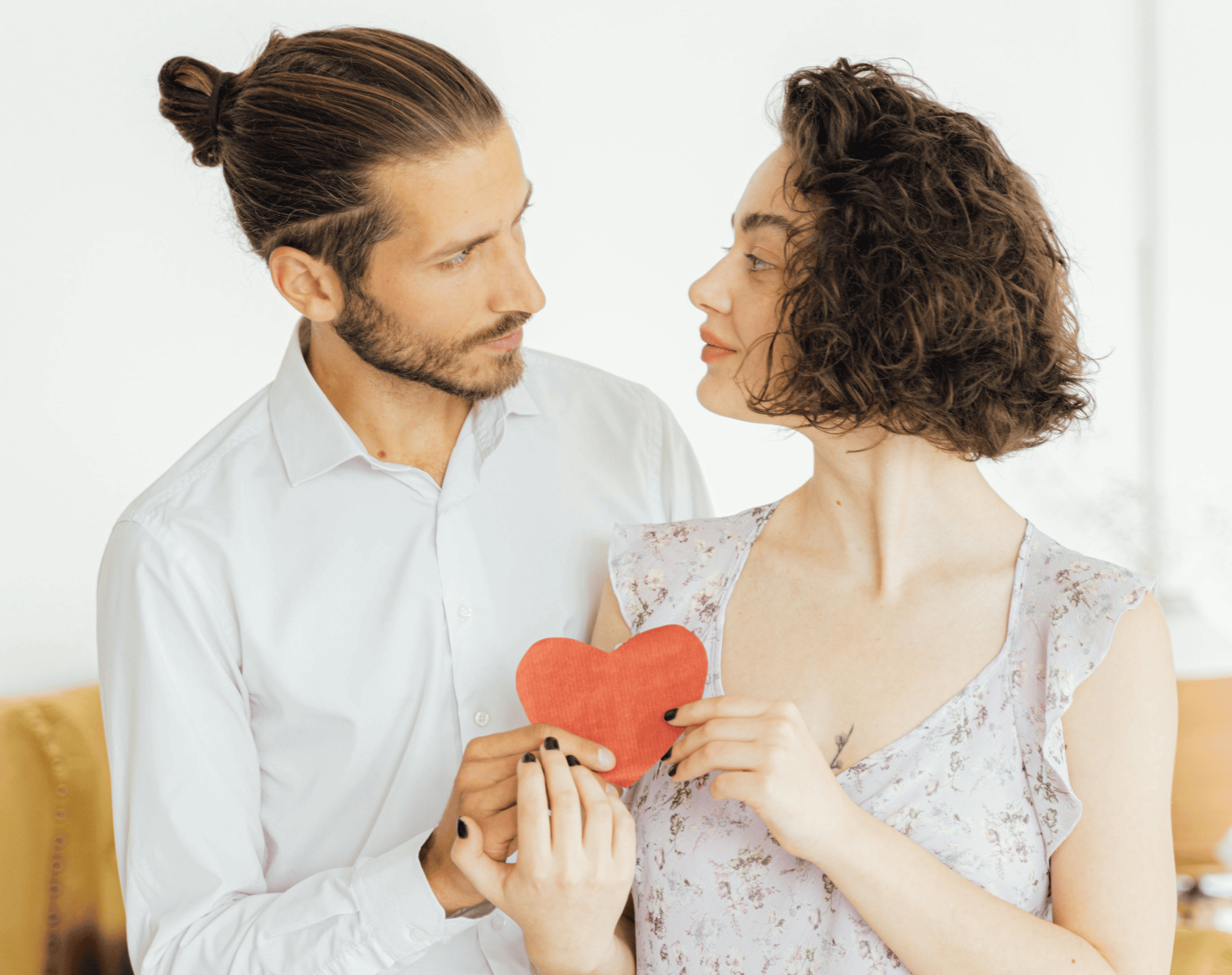 A man stares lovingly at a woman while they both carry a red paper heart between them